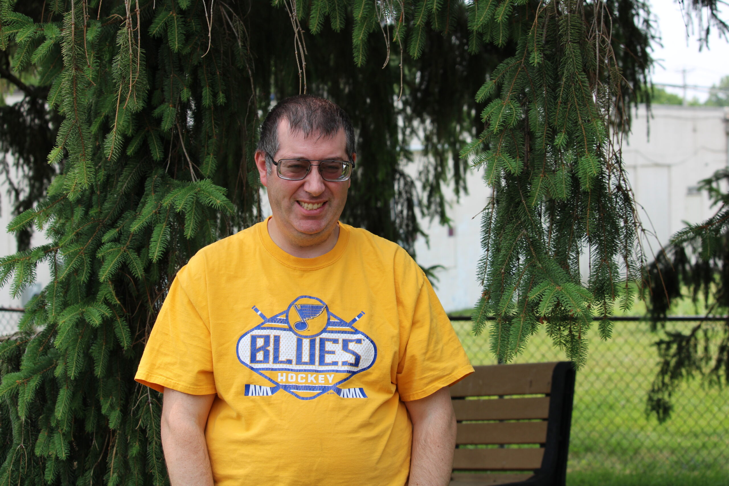 Chris wearing a St. Louis Blues shirt and standing by a tree